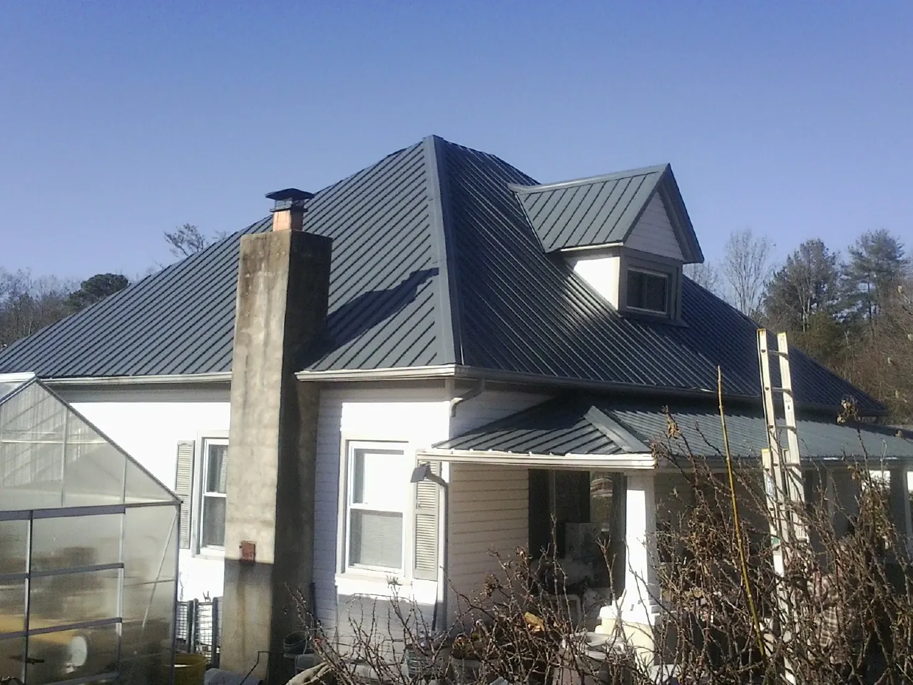 Dark blue standing seam metal roof on a white farmhouse with dormer — Slate & Tile Roof Repair by Roofing Brothers in Teterboro