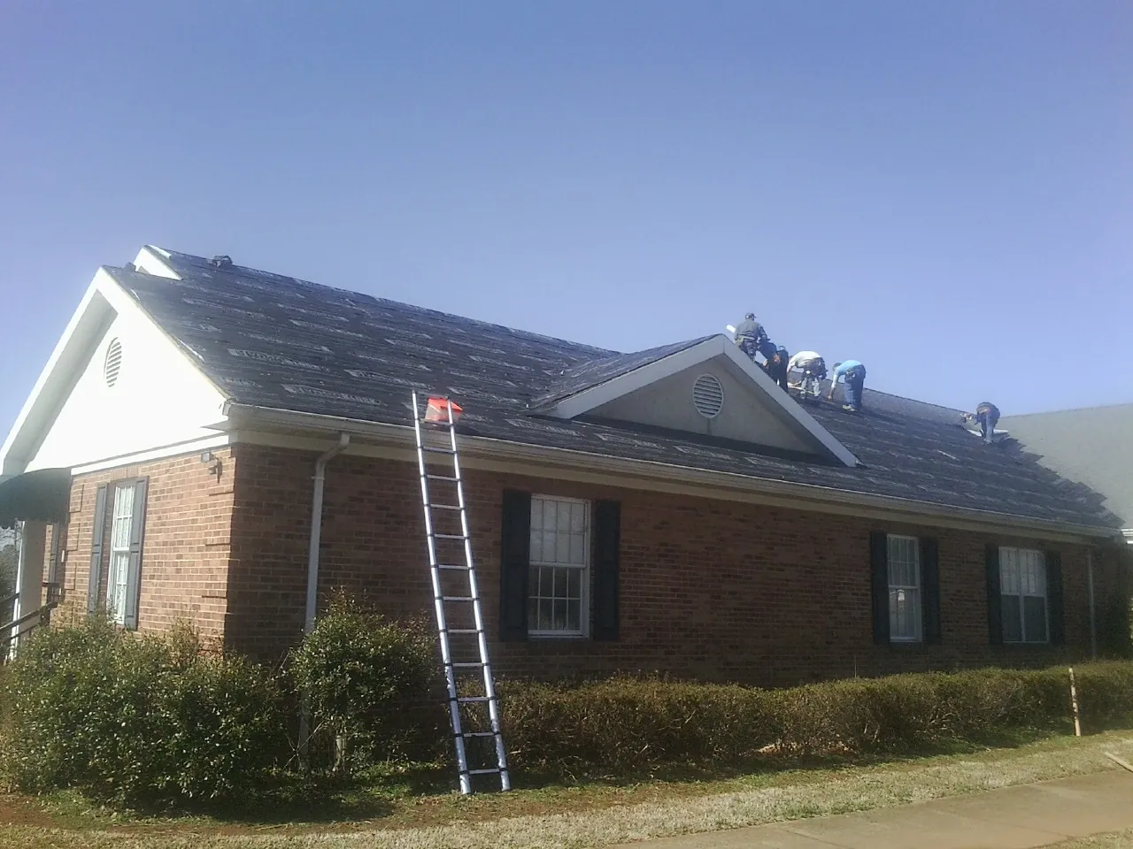 Crew tearing shingles off a brick ranch roof with a ladder set — Metal Roof Repair work by our crew in Teterboro