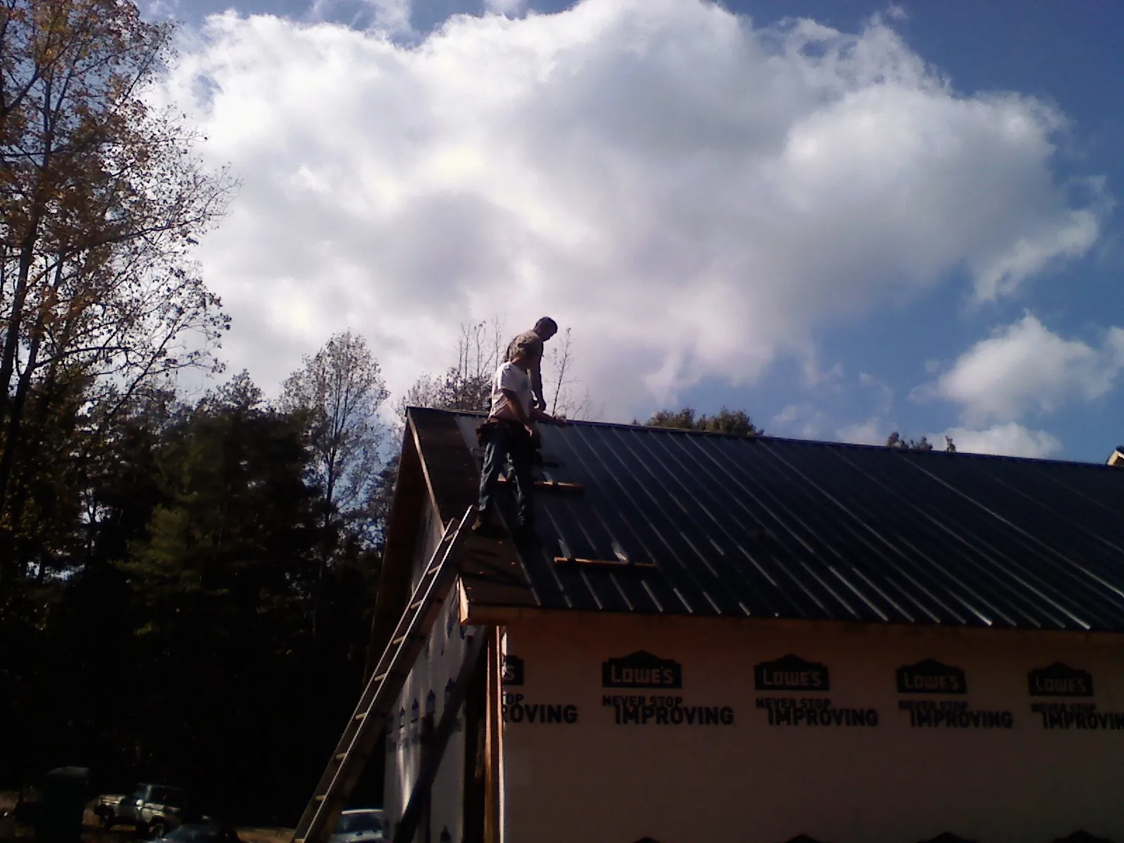 Roofer fastening dark metal panels high against a cloudy sky, from a Roof Inspection job in Teterboro