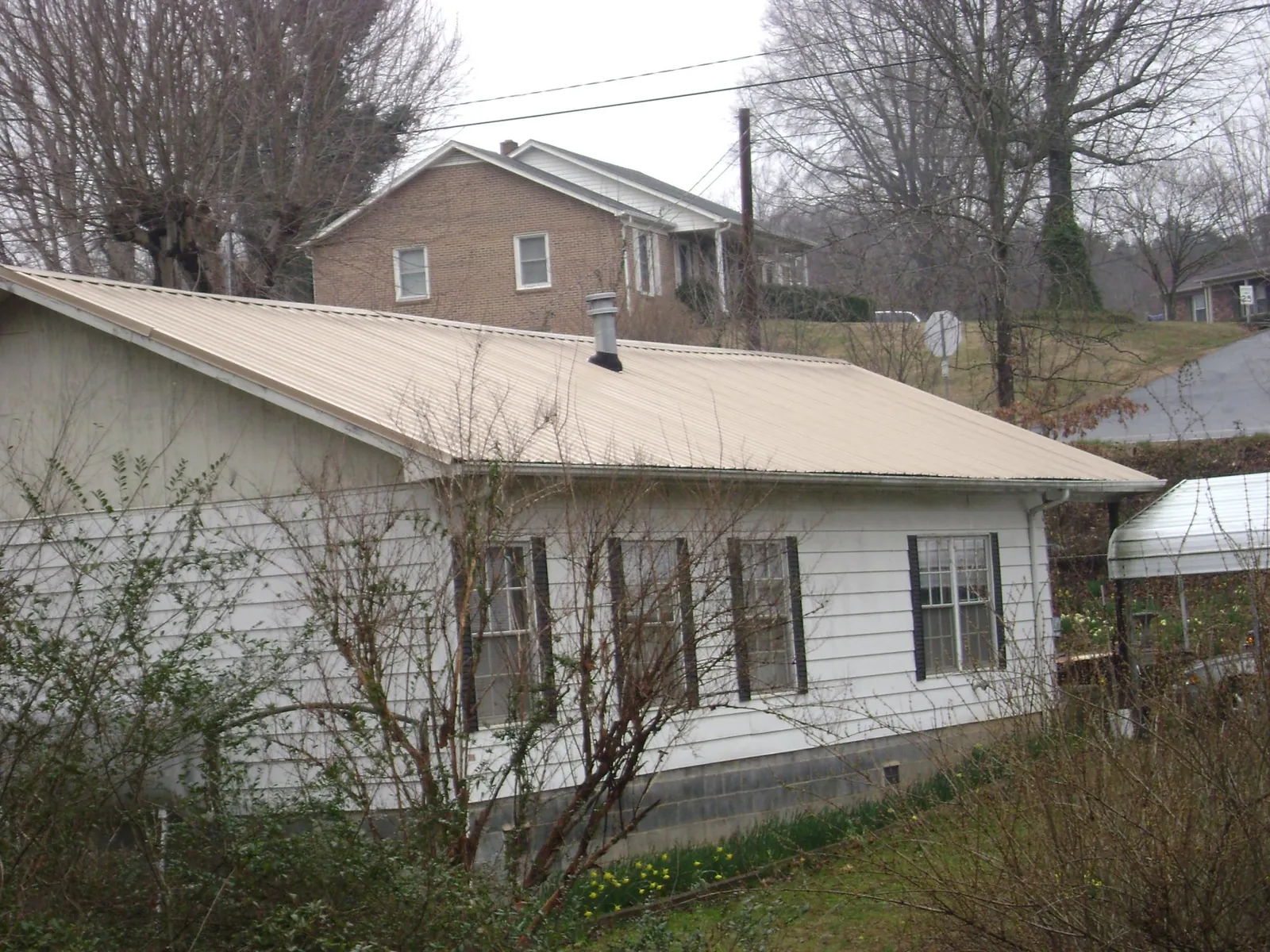 Tan metal roof on a white sided house set into a hillside — Commercial Roofing by Roofing Brothers in Teterboro